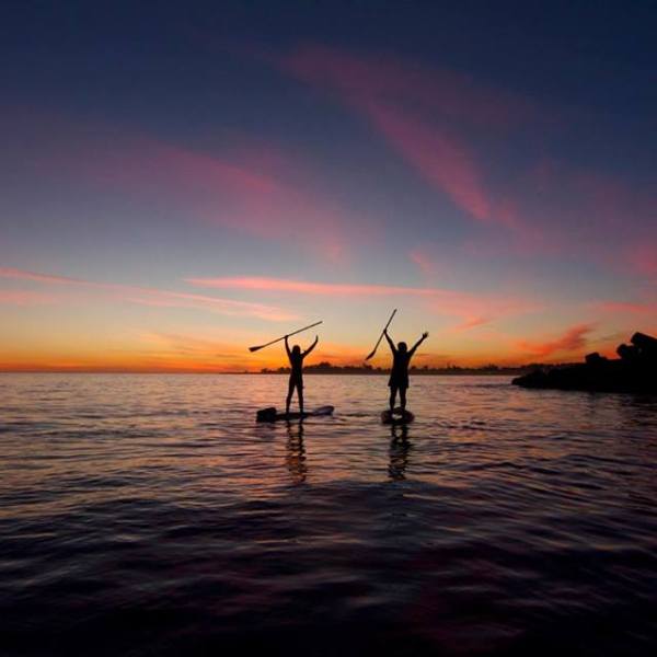 2 paddle boarders raising their hands in the sunset