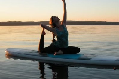 Person doing yoga on paddleboard at sunset on calm water.