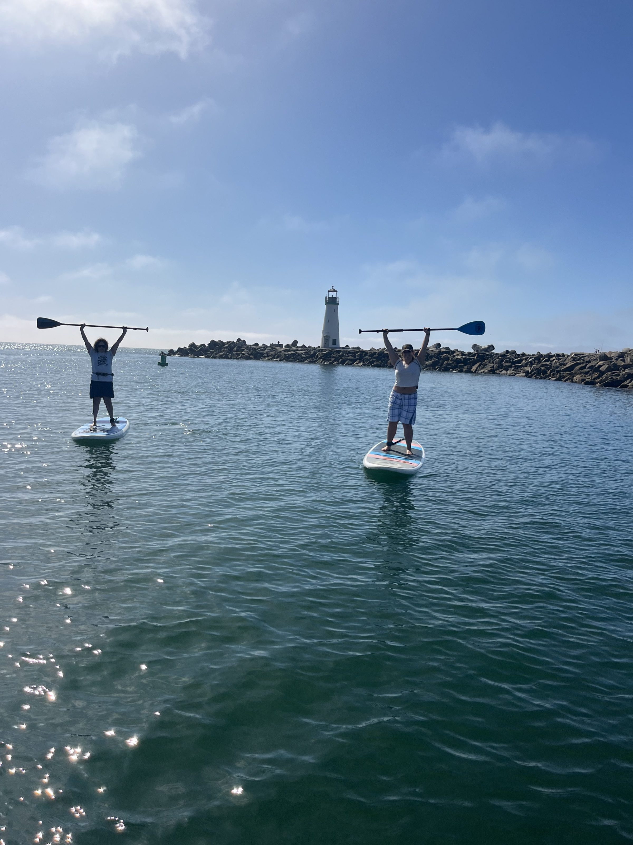 Two people paddleboarding on calm water near a lighthouse.